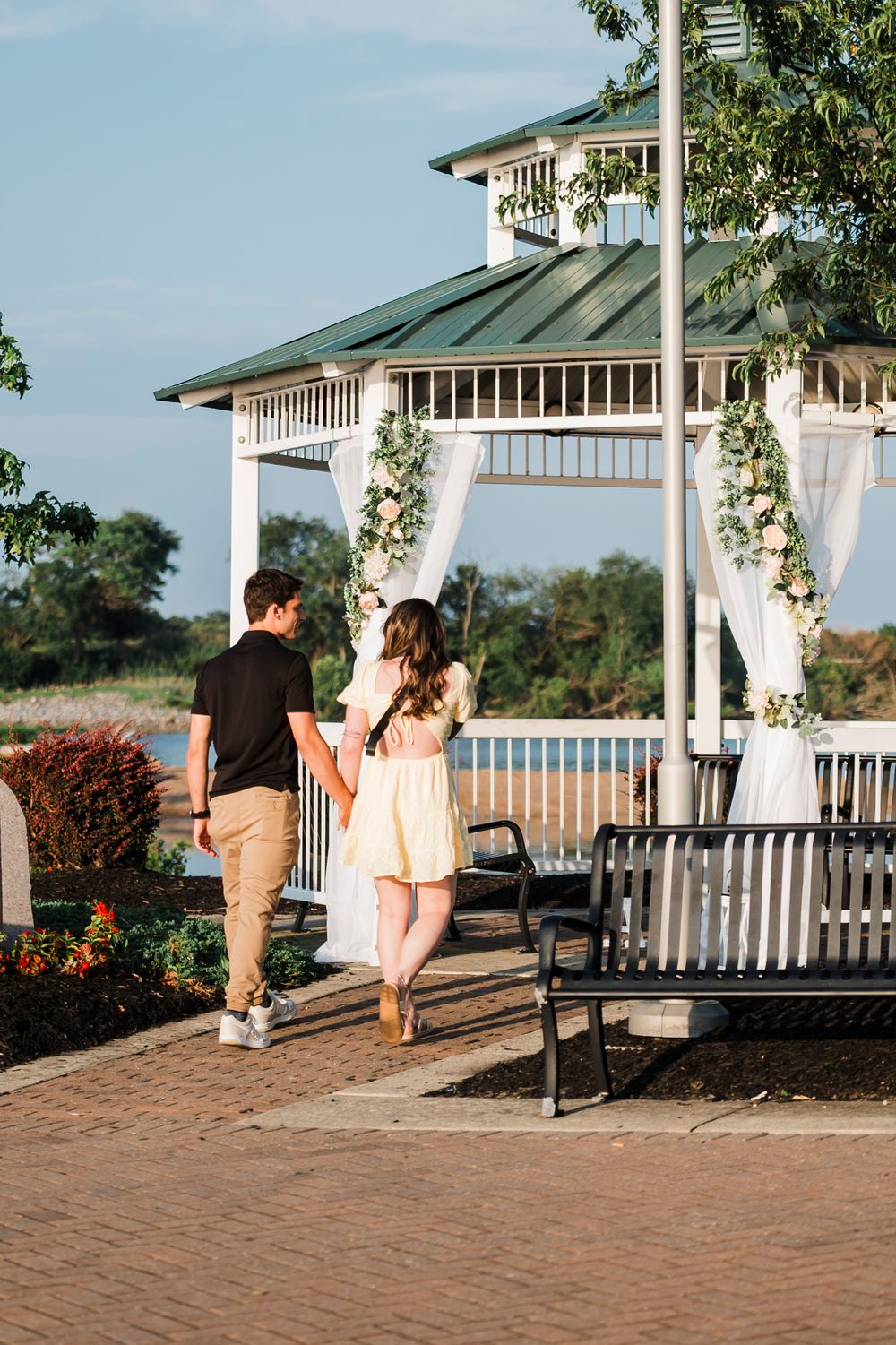 A romantic couple strolls along a waterfront gazebo walkway during sunset.