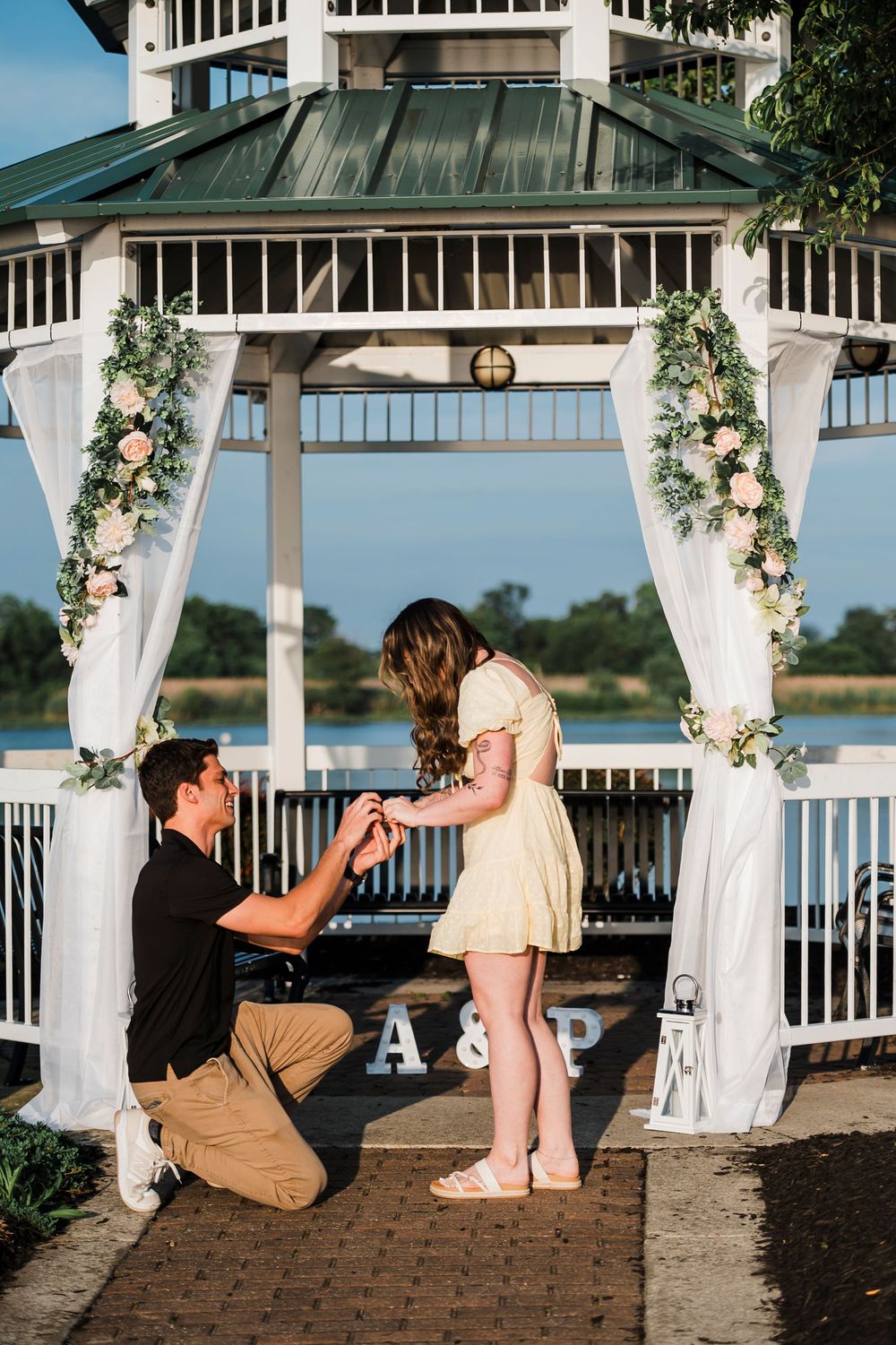 A couple shares a special moment in a decorated gazebo overlooking a serene waterfront during sunset.