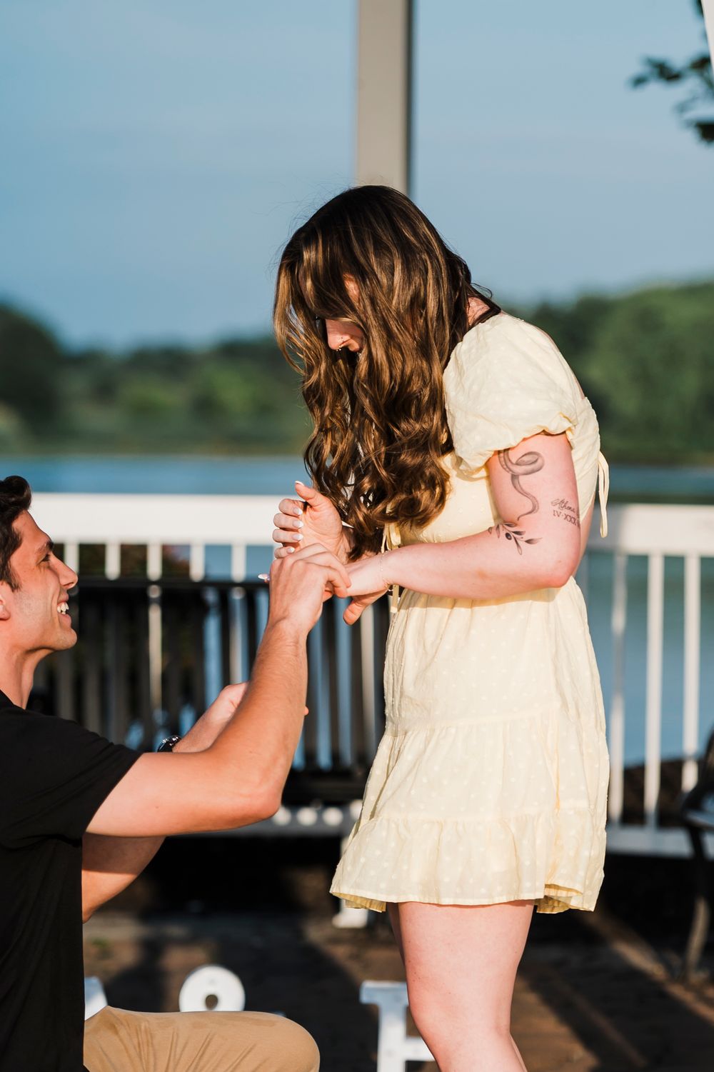 A couple dances together on a wooden deck overlooking a lake at sunset, creating a romantic silhouette.