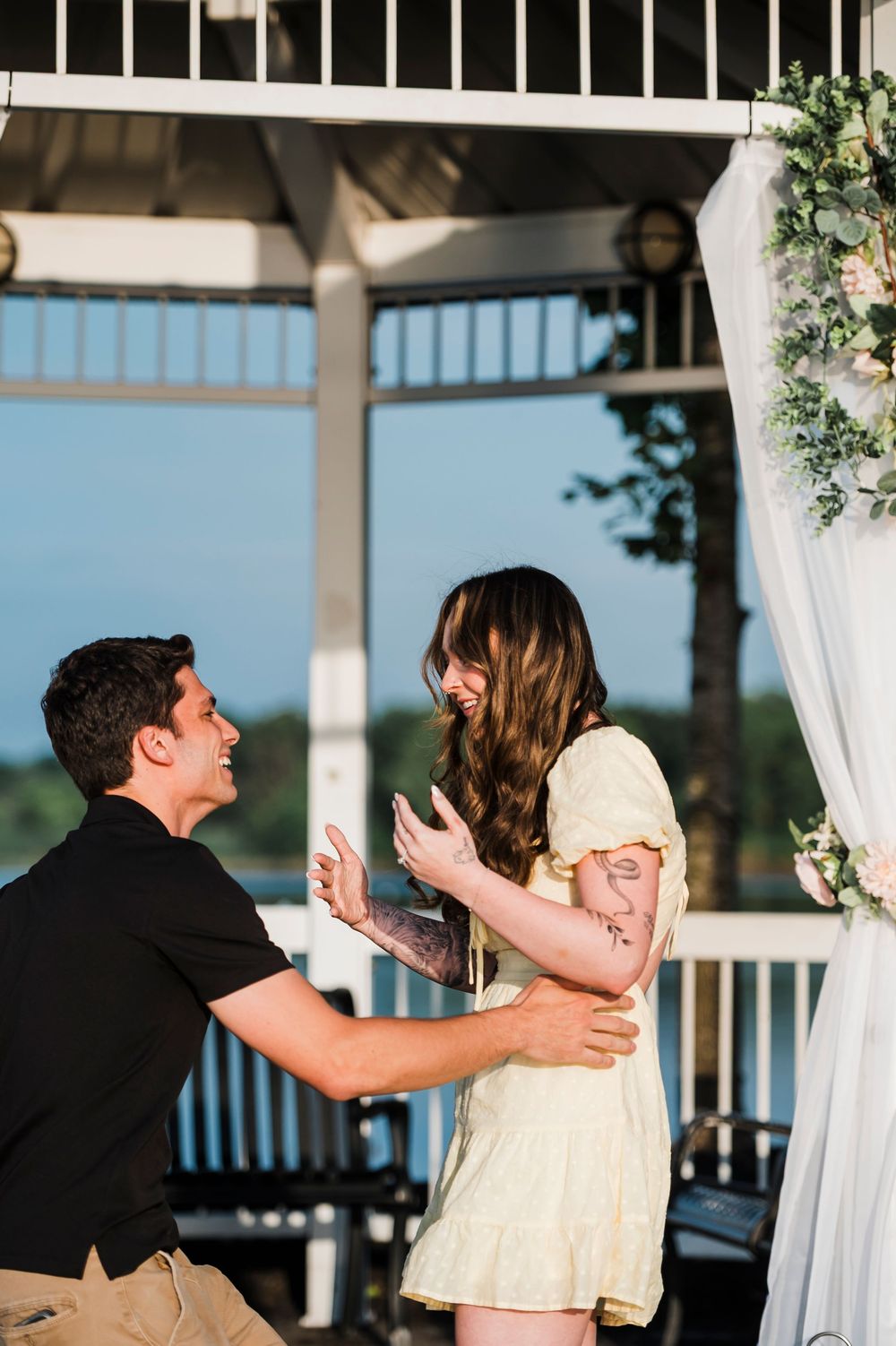 A couple shares a joyful moment together under a decorated white gazebo by the water.