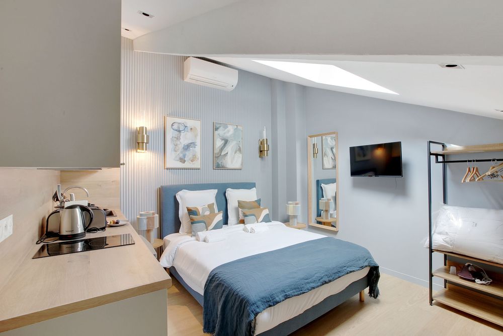 Cozy studio room with blue upholstered bed, skylight, wall-mounted TV, and compact bunk bed area.