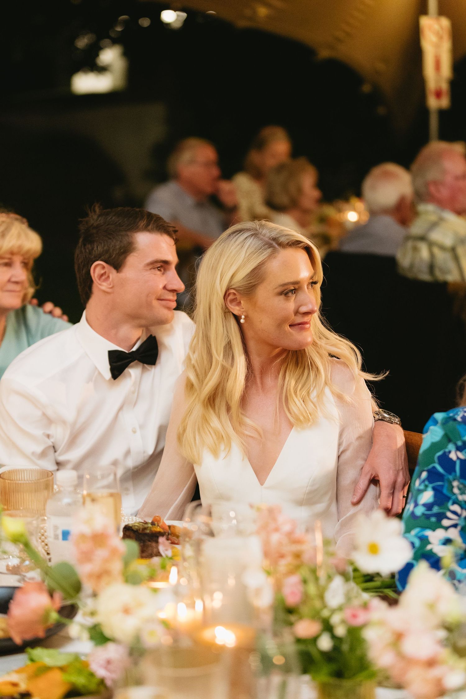 Wedding guests enjoy an elegant dinner reception with candlelit tables decorated with pink floral centerpieces.