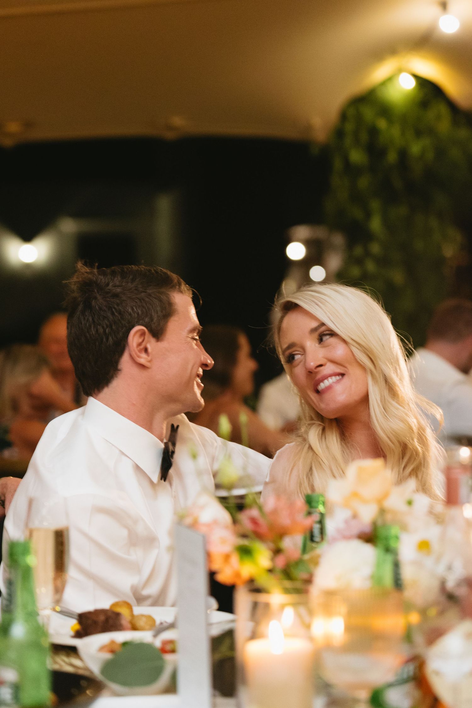 A couple shares a joyful moment while dining at an elegant candlelit table with floral arrangements.