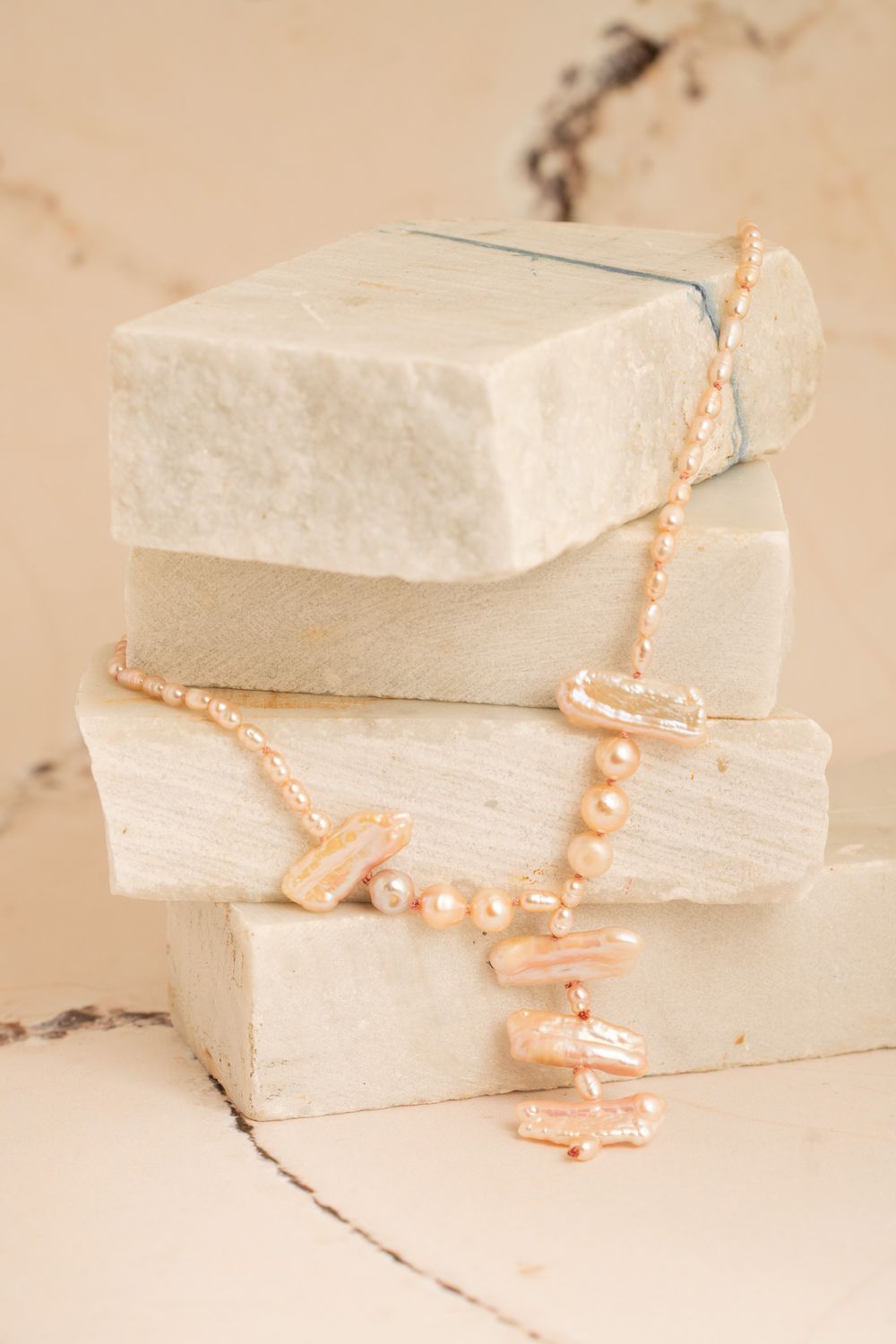 A gold necklace draped over stone props in warm light; Tuscan-inspired brand imagery for international lifestyle and accessory lines.