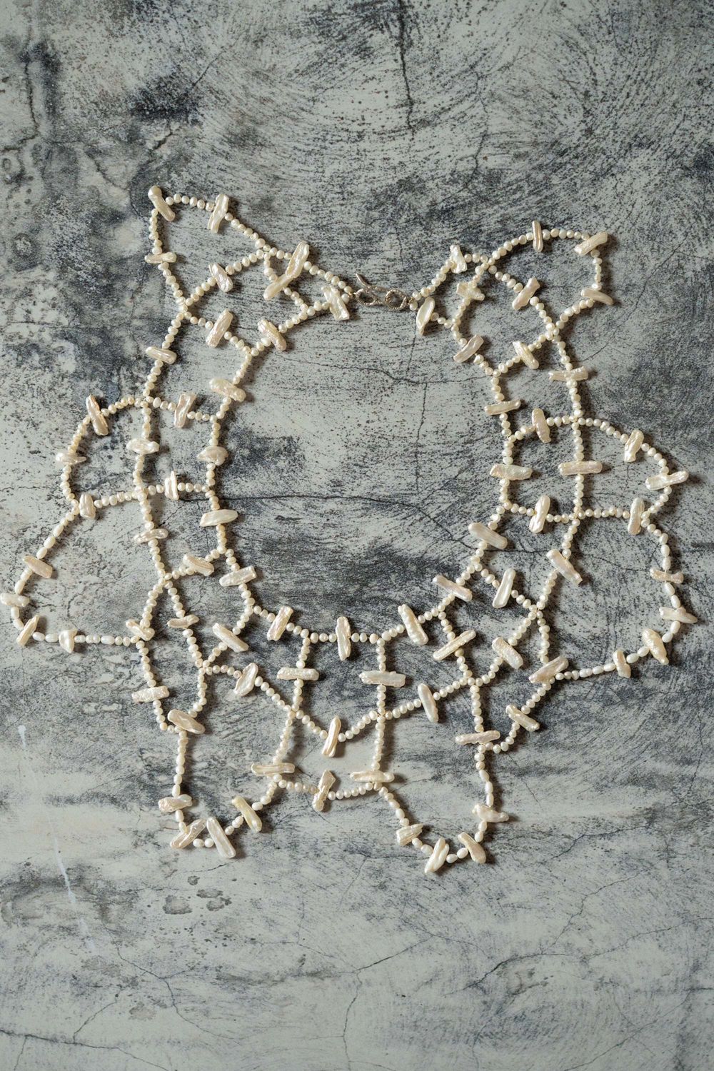 Overhead shot of an intricate beaded necklace on a grey surface; professional jewelry photography service for international e-commerce.Overh
