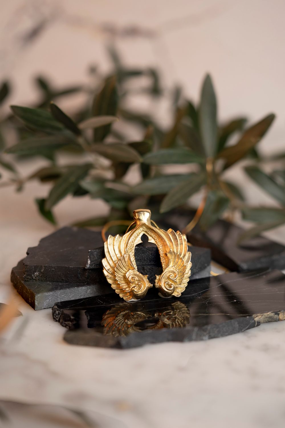 Gold leaf-shaped earrings on a marble surface with greenery; luxury jewelry lookbook photography shot in Florence.