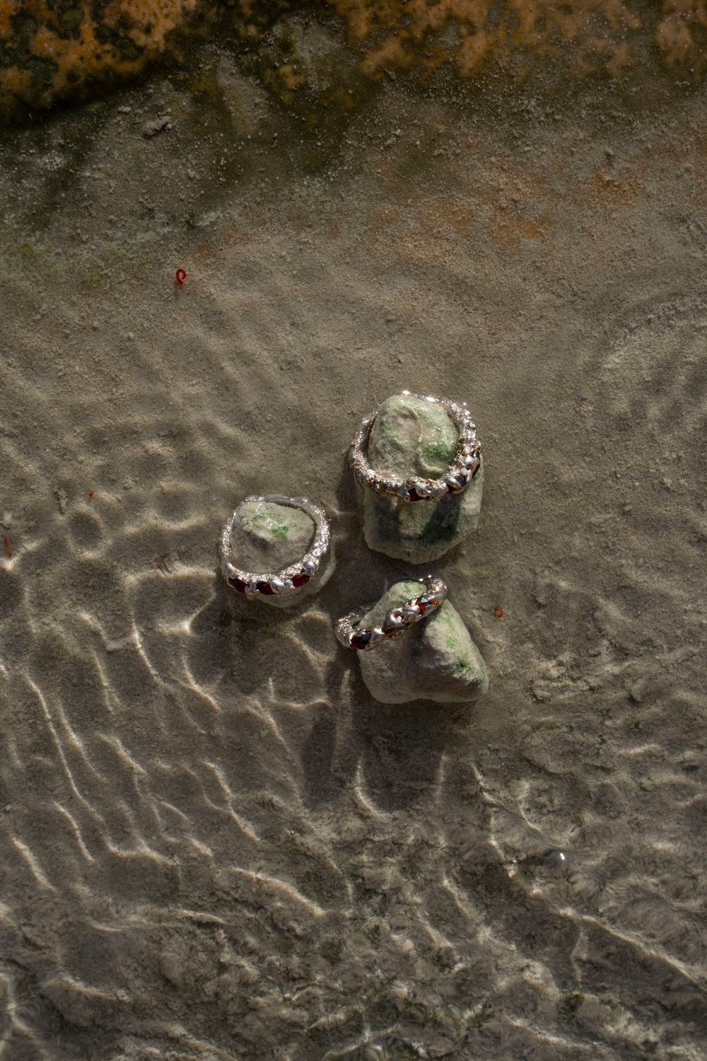 Natural stone jewelry pieces resting in a shallow stream; on-location product photography and scouting in the Tuscan countryside.