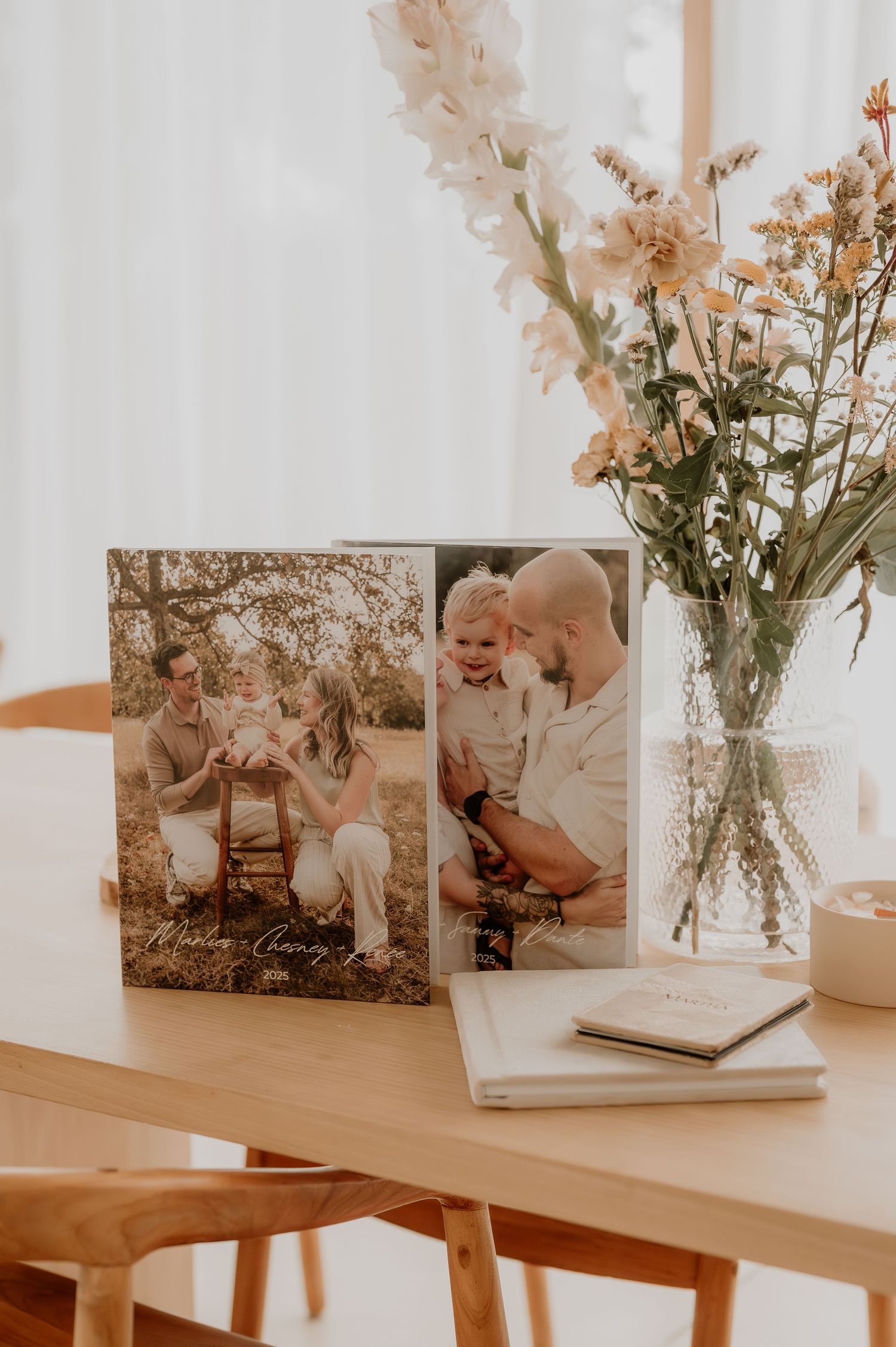 Fotodisplay op een houten tafel met verse bloemen in een vaas en ingelijste familiefoto’s, vastgelegd in zacht natuurlijk licht.