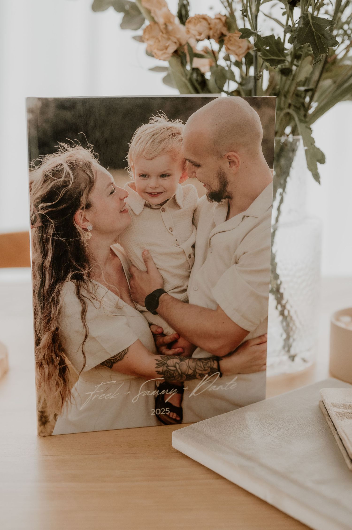 Familiefotodisplay met een bloemstuk en ingelijste portretten op een houten tafel, vastgelegd in zacht natuurlijk licht.