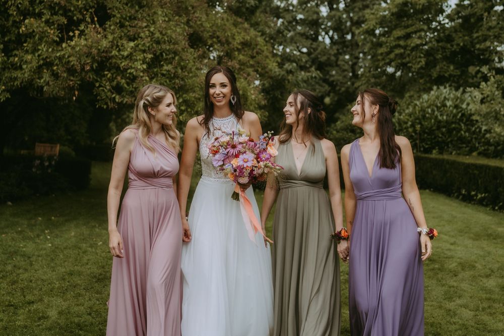Bridesmaids in pastel dresses gather around bride in outdoor garden setting.