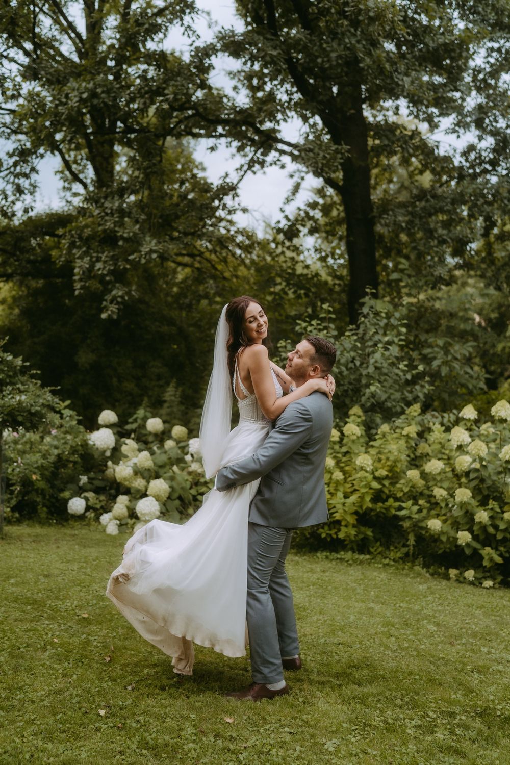 A romantic dance moment on a green lawn with hydrangea bushes in the background.