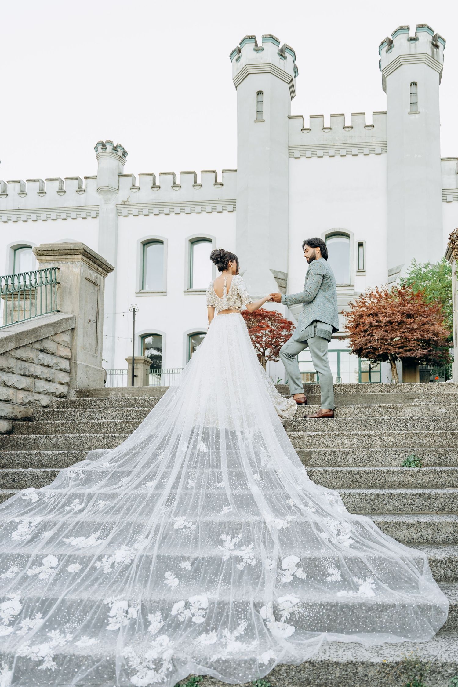 A flowing white wedding dress with a long cathedral veil cascading down stone steps of a castle.