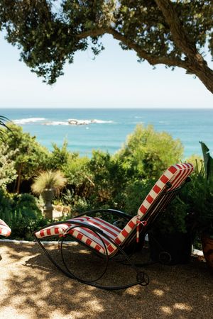 Striped lounge chairs overlook a scenic ocean view through tropical trees and foliage.