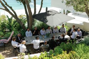 Group of people enjoying an outdoor gathering in a lush garden setting with white furniture.