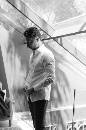 A person in a white shirt and dark pants stands near a glass window structure in a bright architectural space.