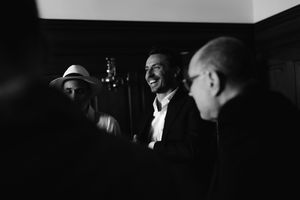 A black and white candid photograph shows three people in conversation at what appears to be a social gathering.