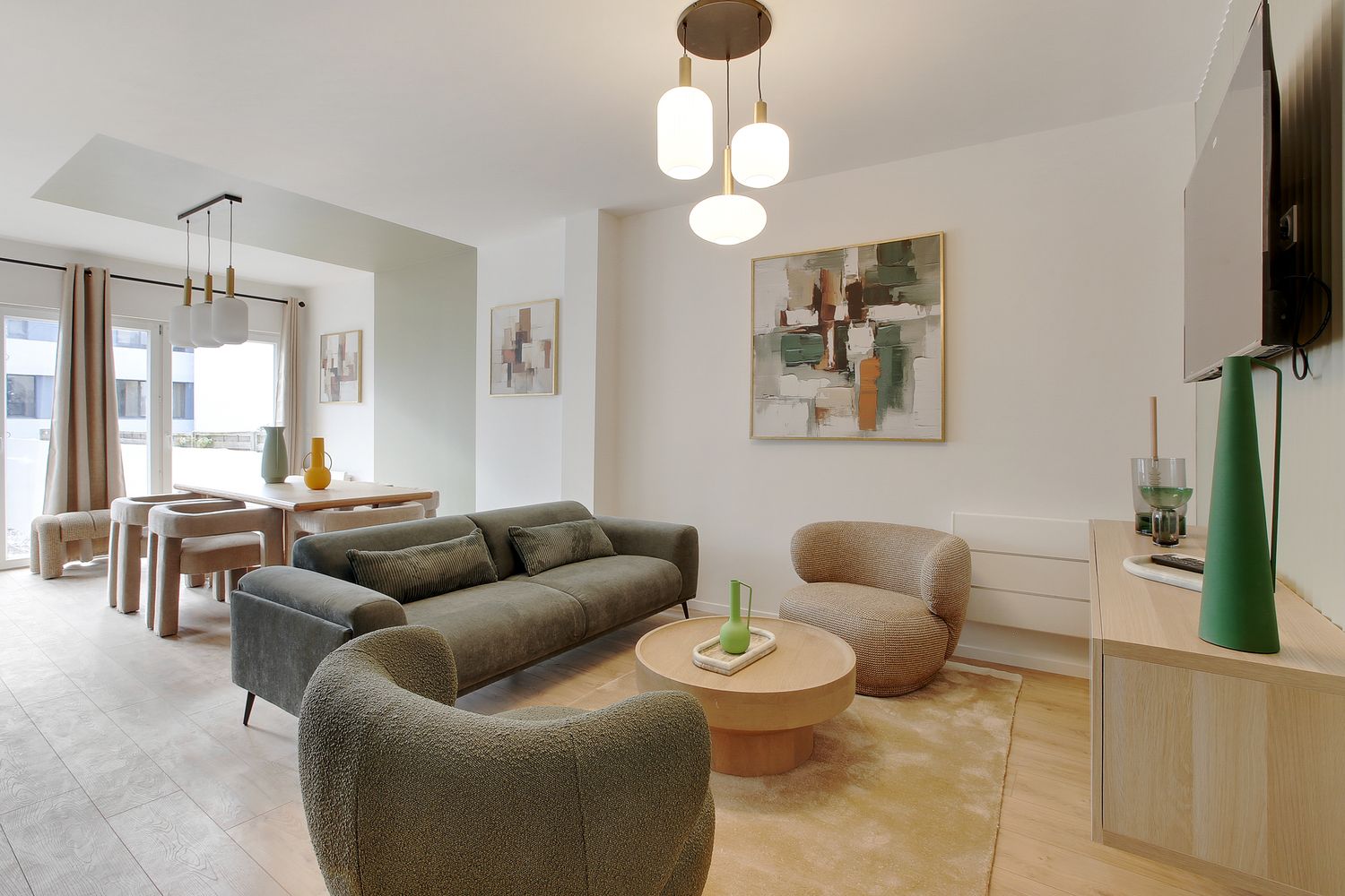 Contemporary living room with green velvet sofas, round coffee table, pendant lights, and dining area.
