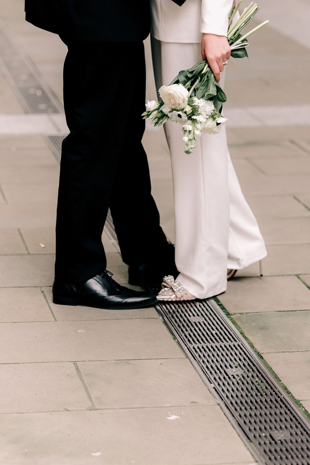 Wedding couple's feet walking on tiled floor with white dress and black shoes visible.