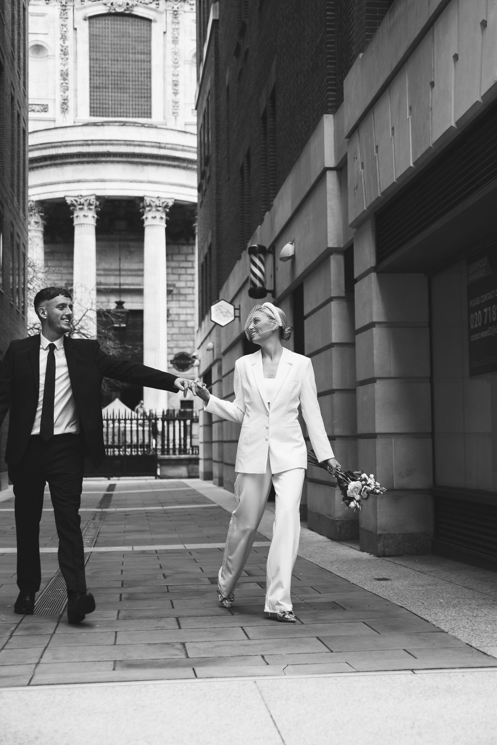 Couple in contrasting black and white outfits walking through a classical columned corridor.