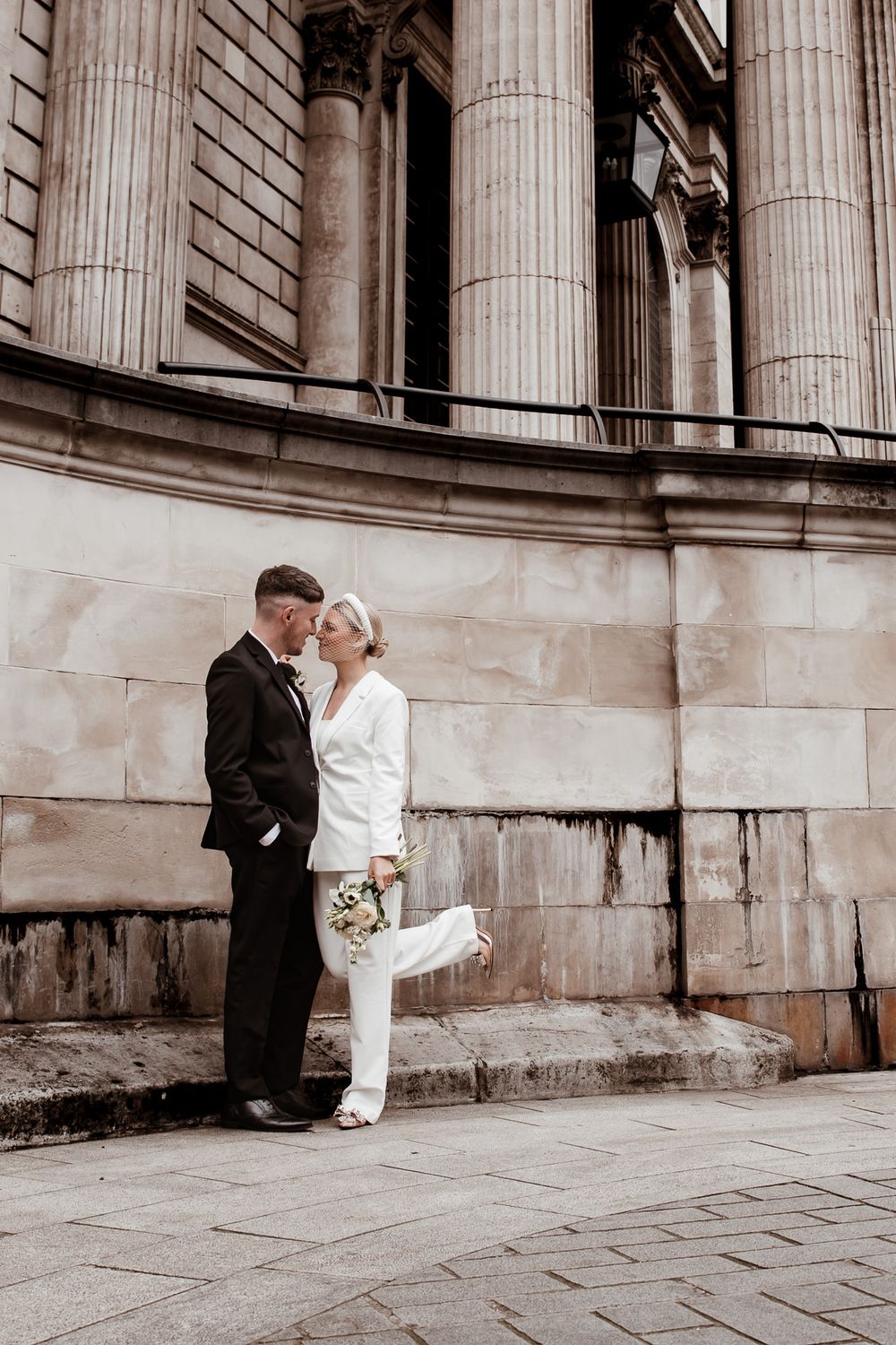 Romantic wedding couple poses against classic stone columns in elegant black and white photography sequence.