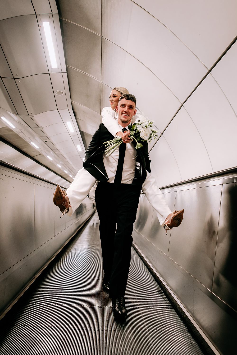 Wedding couple walking through London underground tunnel with geometric lighting.