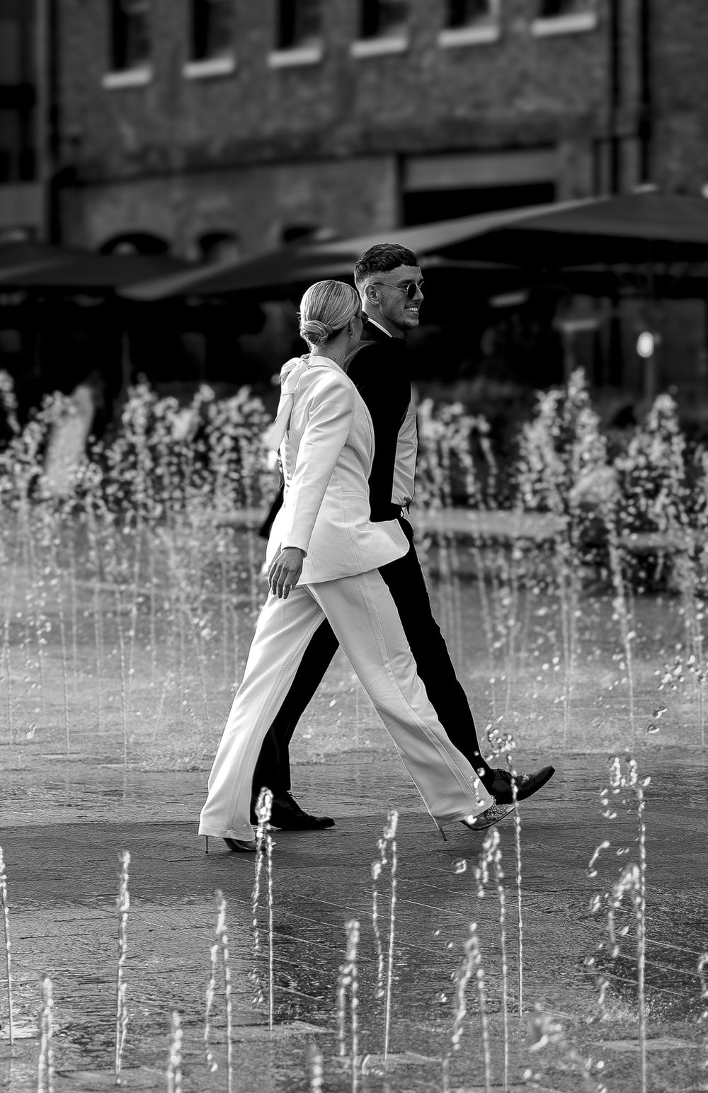 Couple walking through modern water fountain display in black and white.