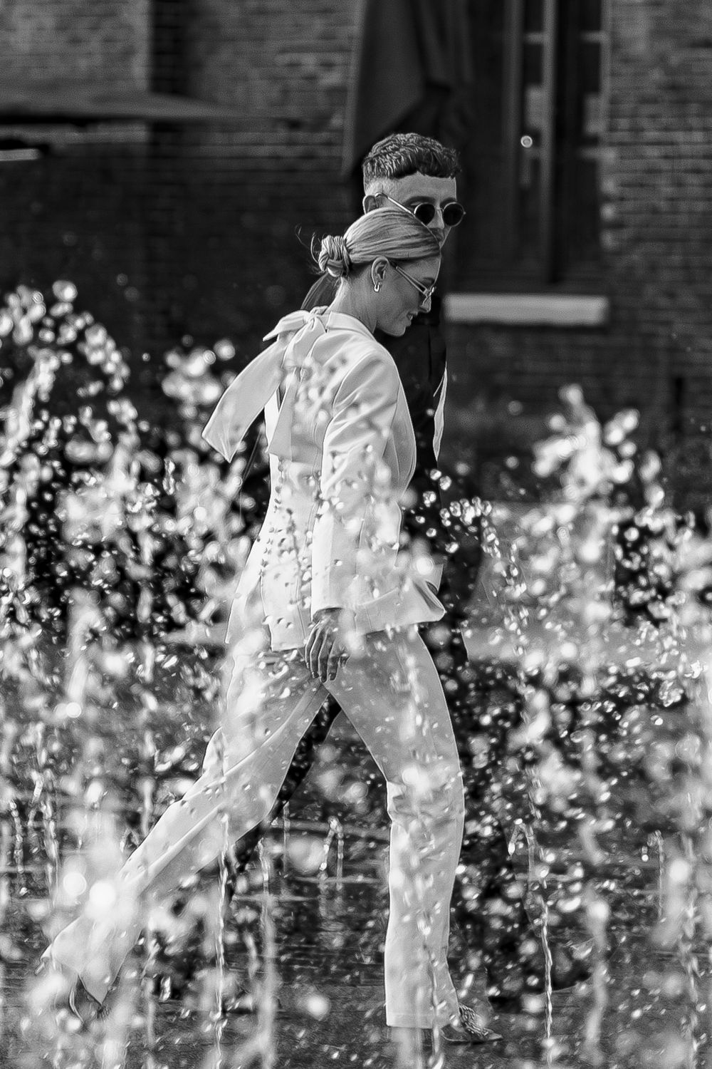 People walking through spraying water fountains in urban setting.