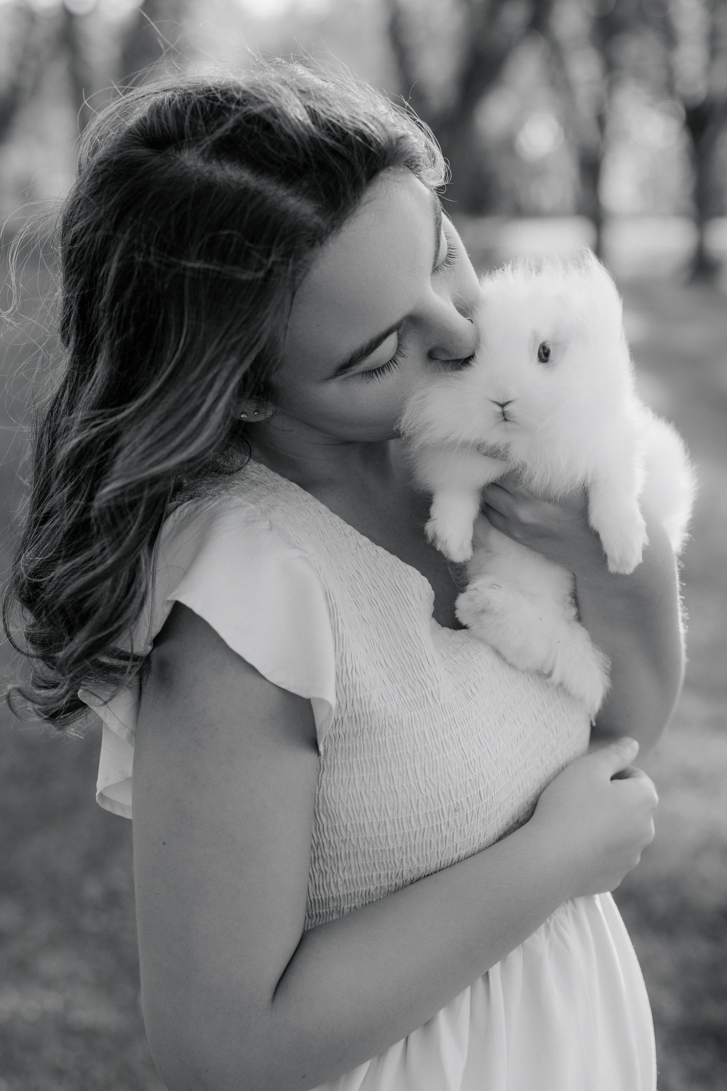 A tender moment captured in black and white as someone in a white dress cuddles an adorable fluffy white bunny.