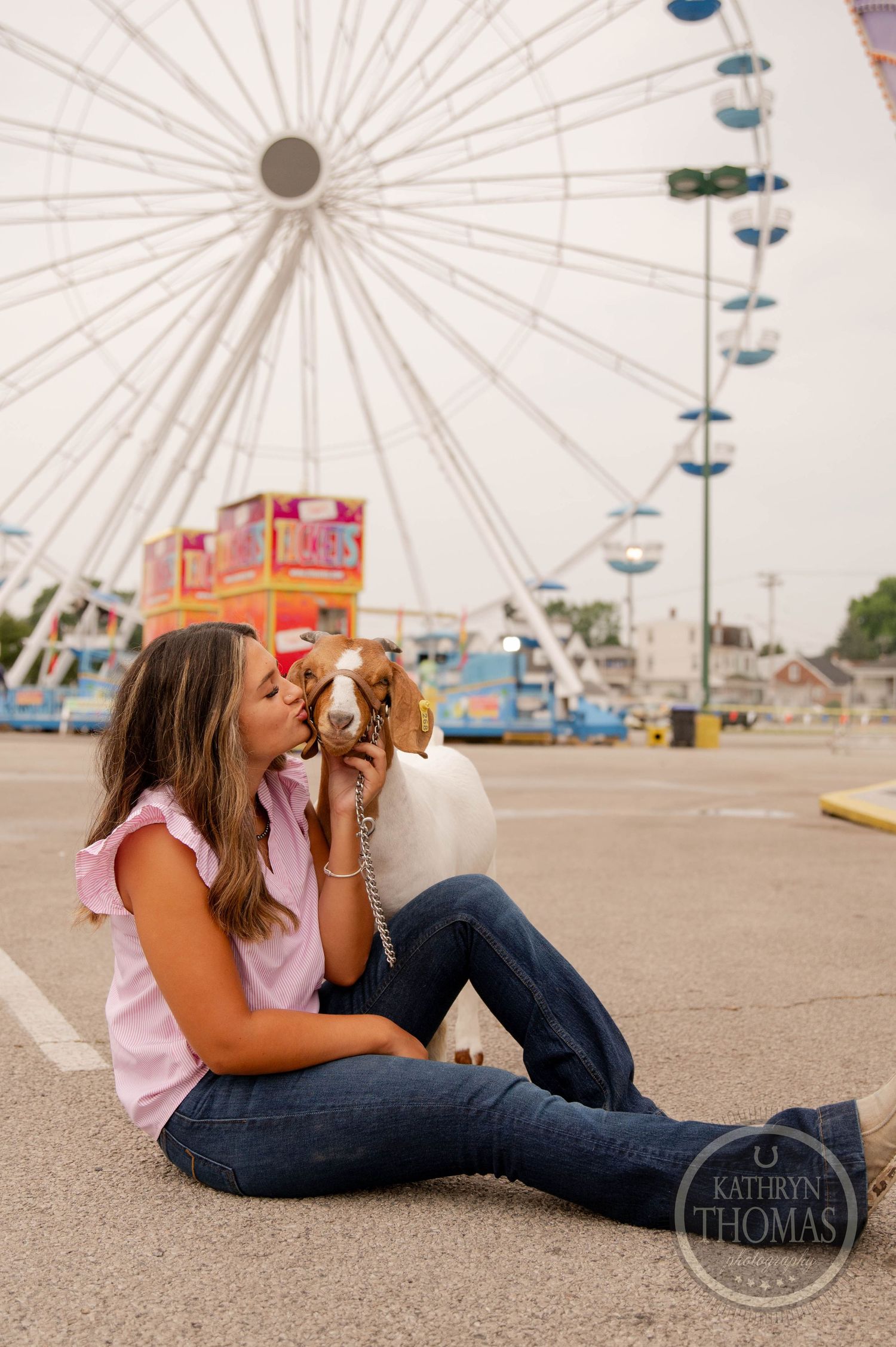 A goat poses in front of a large ferris wheel at a carnival fairground.