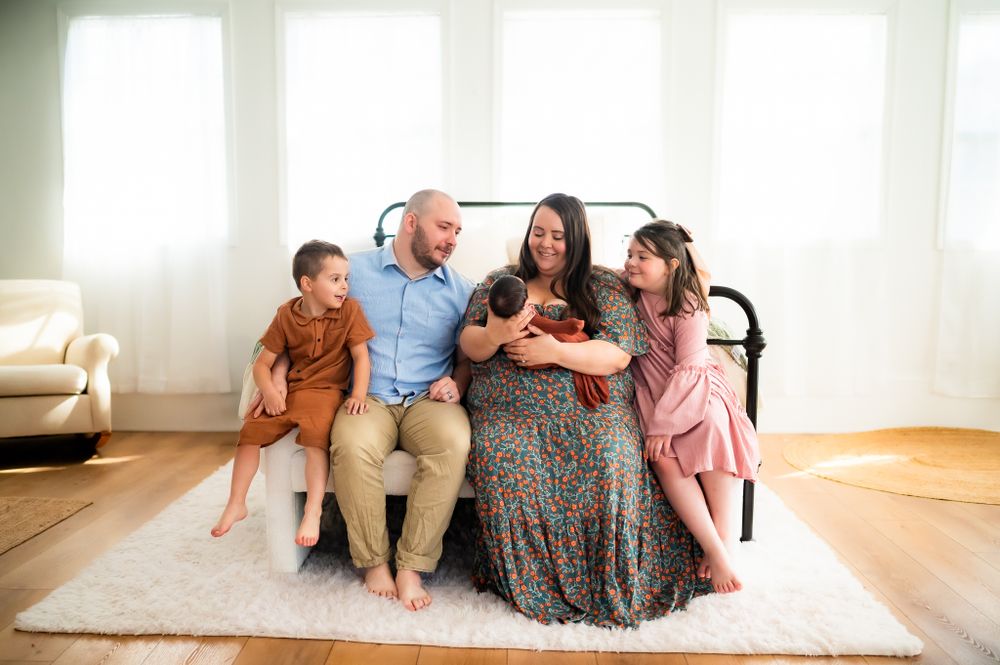 A relaxed family sits together on a white rug in a bright, sunlit living room interior.