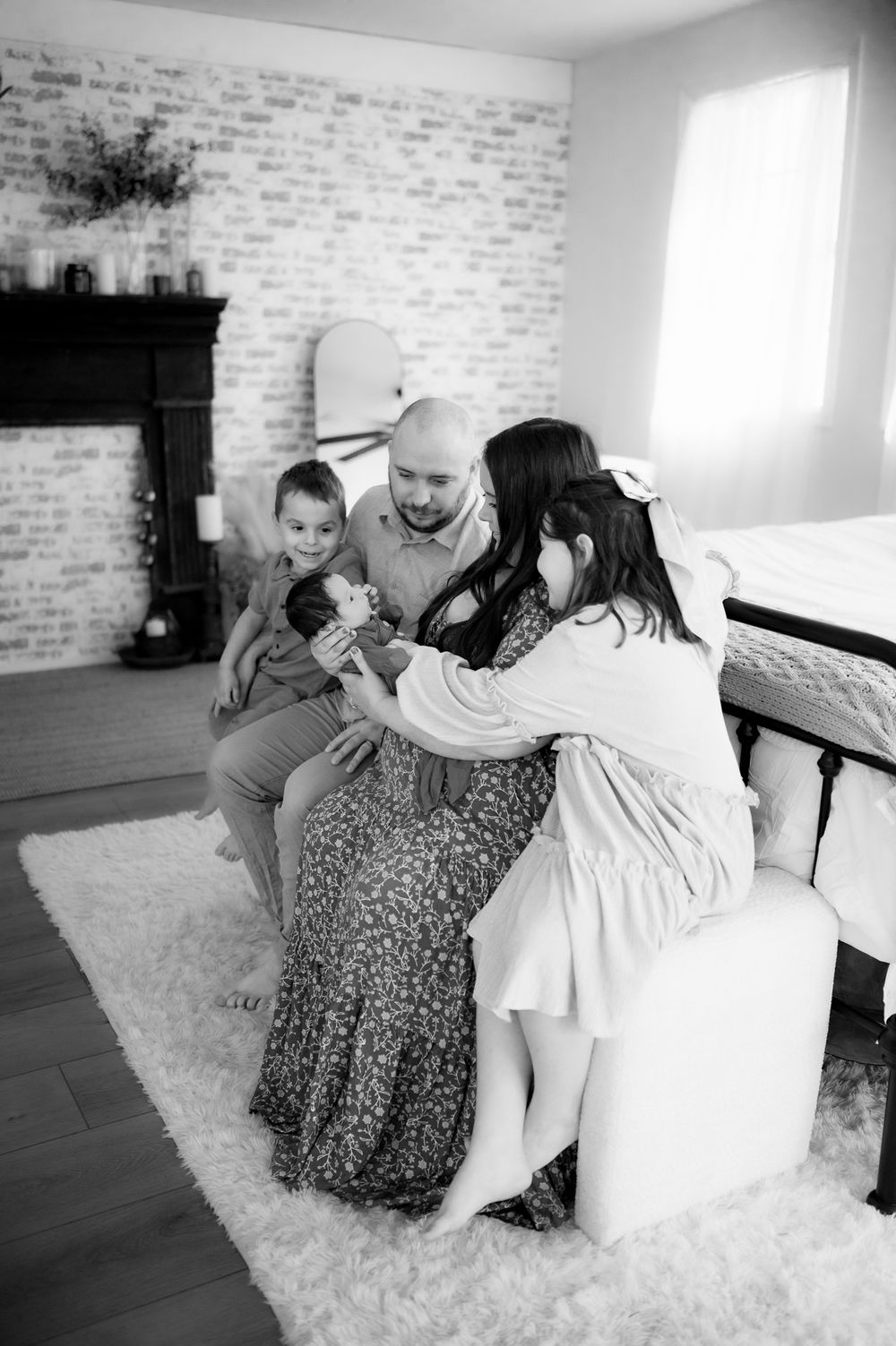 Family gathers on white rug in cozy living room with exposed brick wall and dark wood floors in black and white.