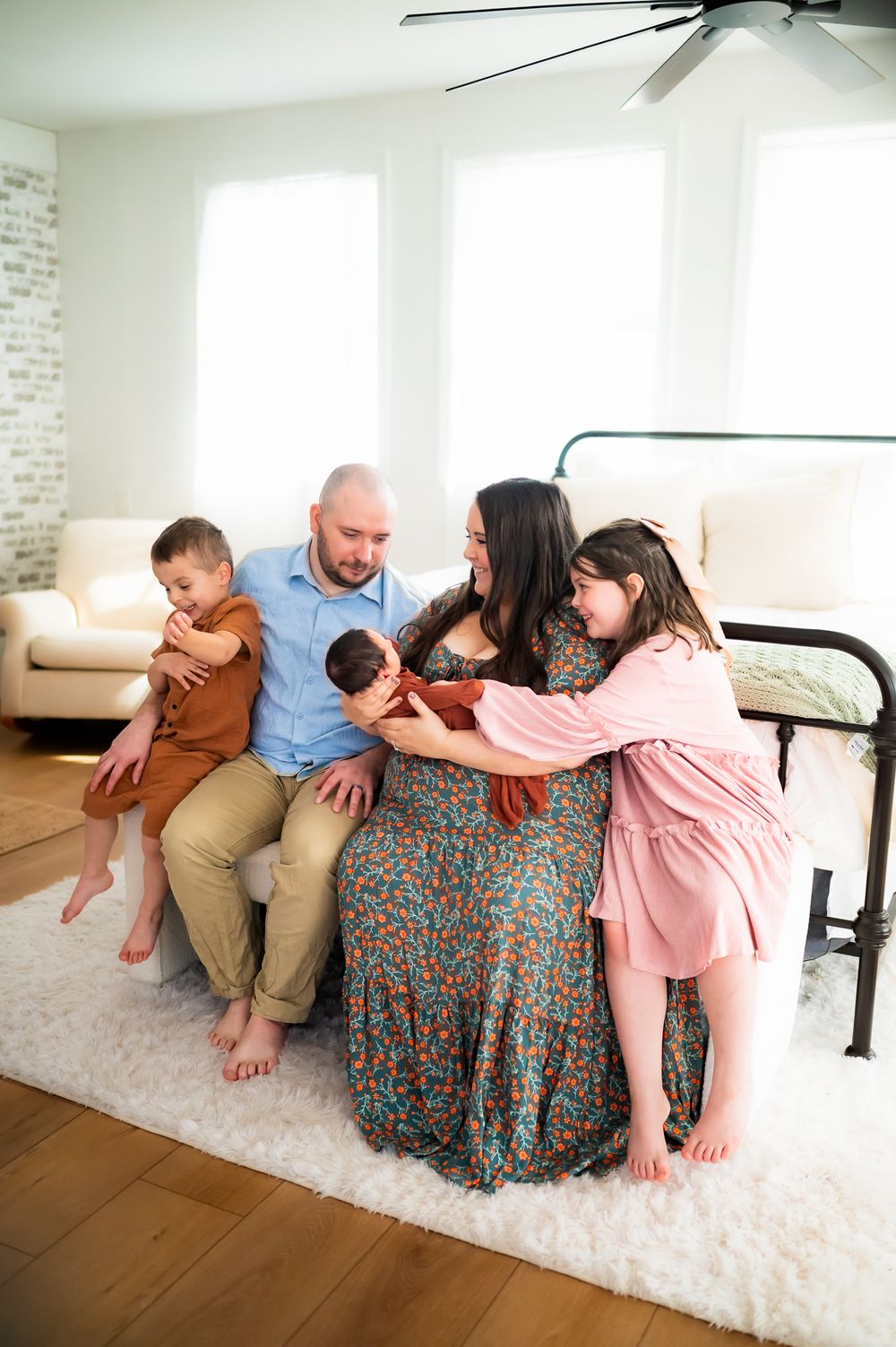 A candid moment of a family of five sitting together on a white rug in a bright, modern living room.