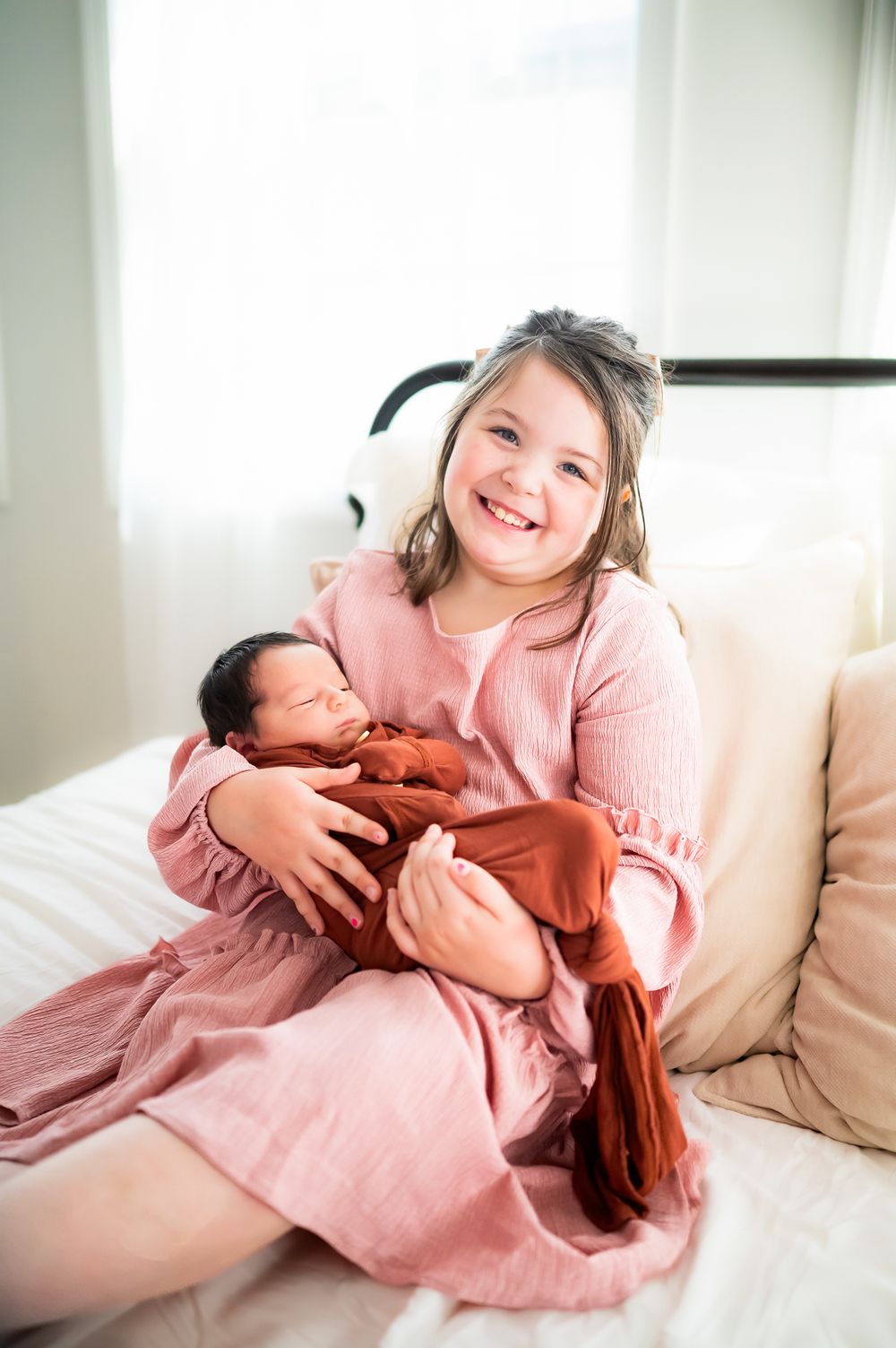 A sweet family moment captured as two people dressed in pink sit together on a couch by a bright window.
