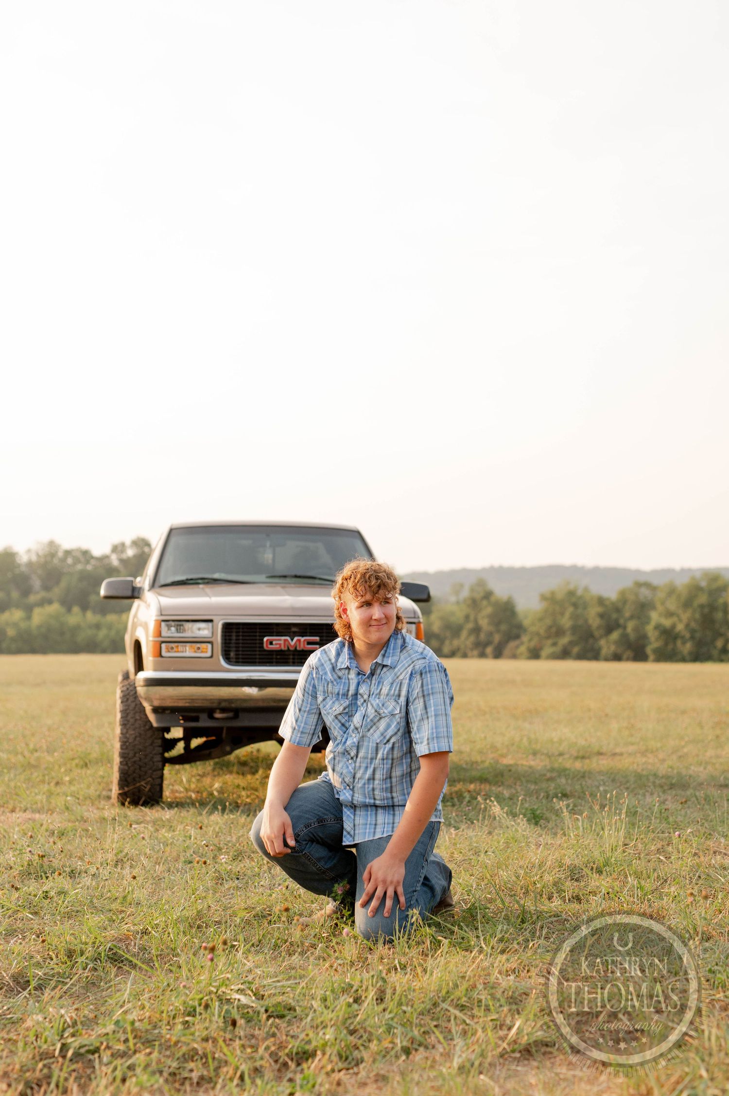 A casual kneeling pose in front of a lifted GMC truck during sunset.