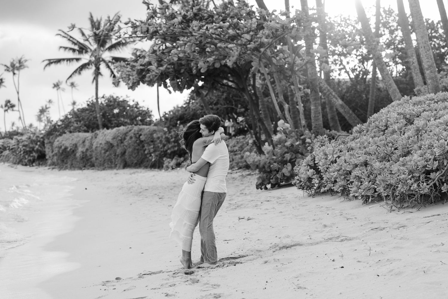A black and white beach photo with palm trees and tropical vegetation in the background.