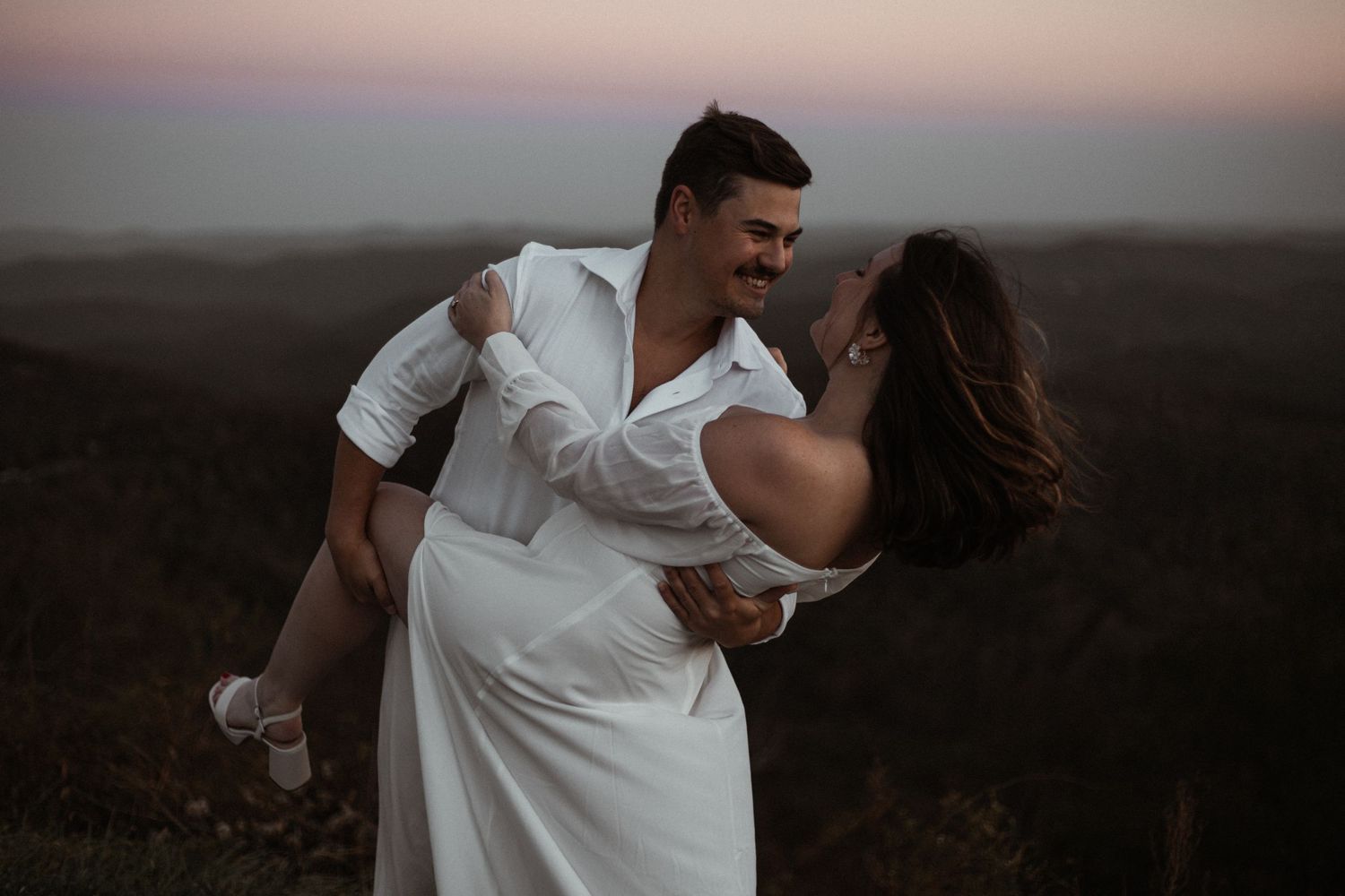 A romantic sunset dance pose with a couple in formal attire on a hilltop.