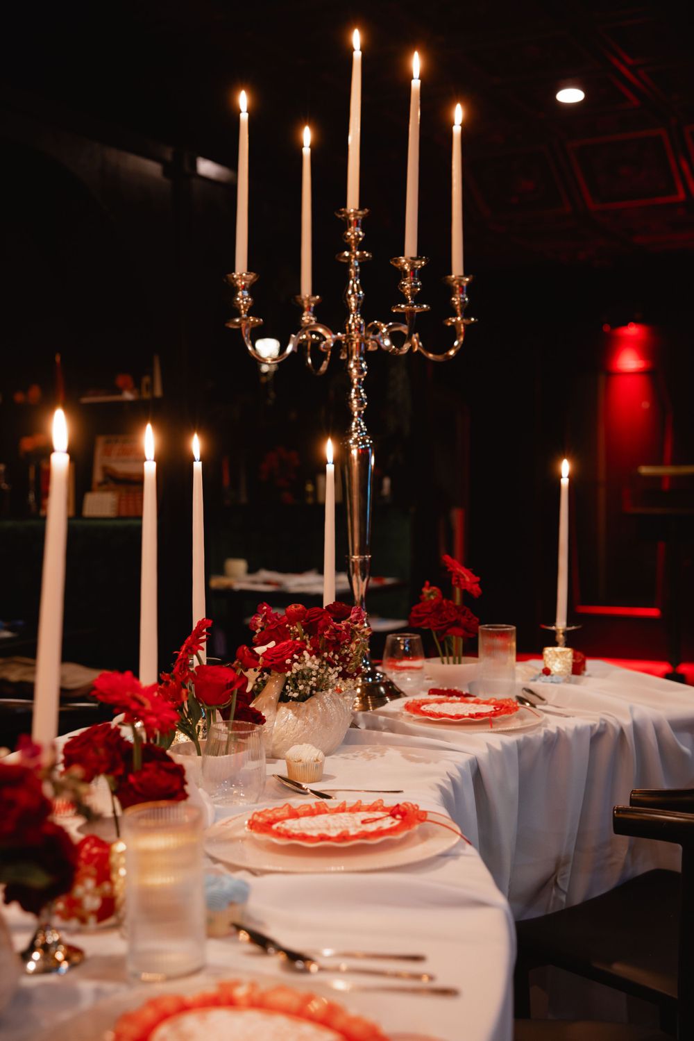 Romantic candlelit wedding table featuring a silver candelabra, red floral arrangements, and red-trimmed place settings.