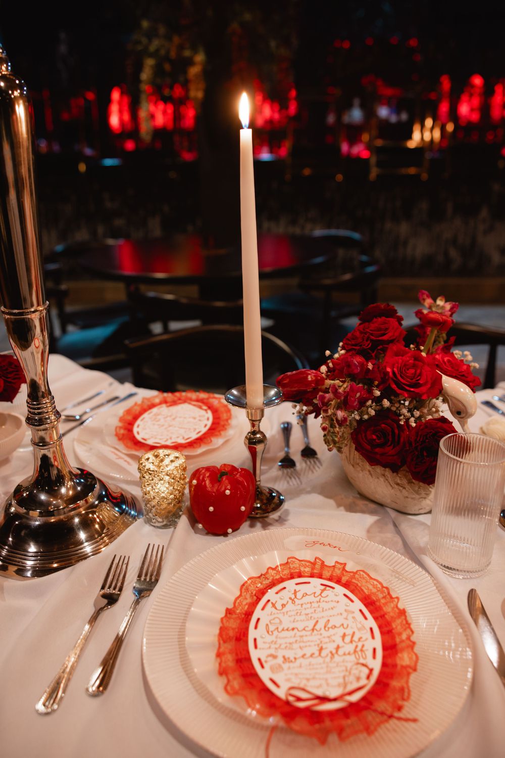 Intimate wedding table setting with tall white candles, red roses centerpiece, and decorative red lace charger plates.