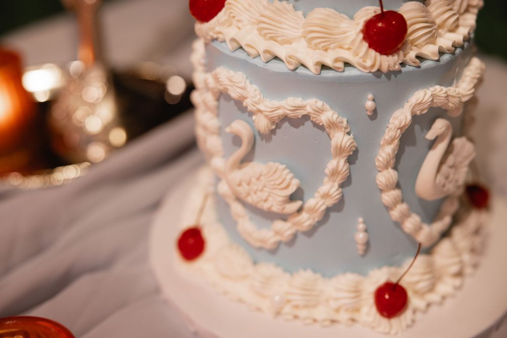 Elegant light blue wedding cake with white swan heart decorations and red cherry accents on two tiers.