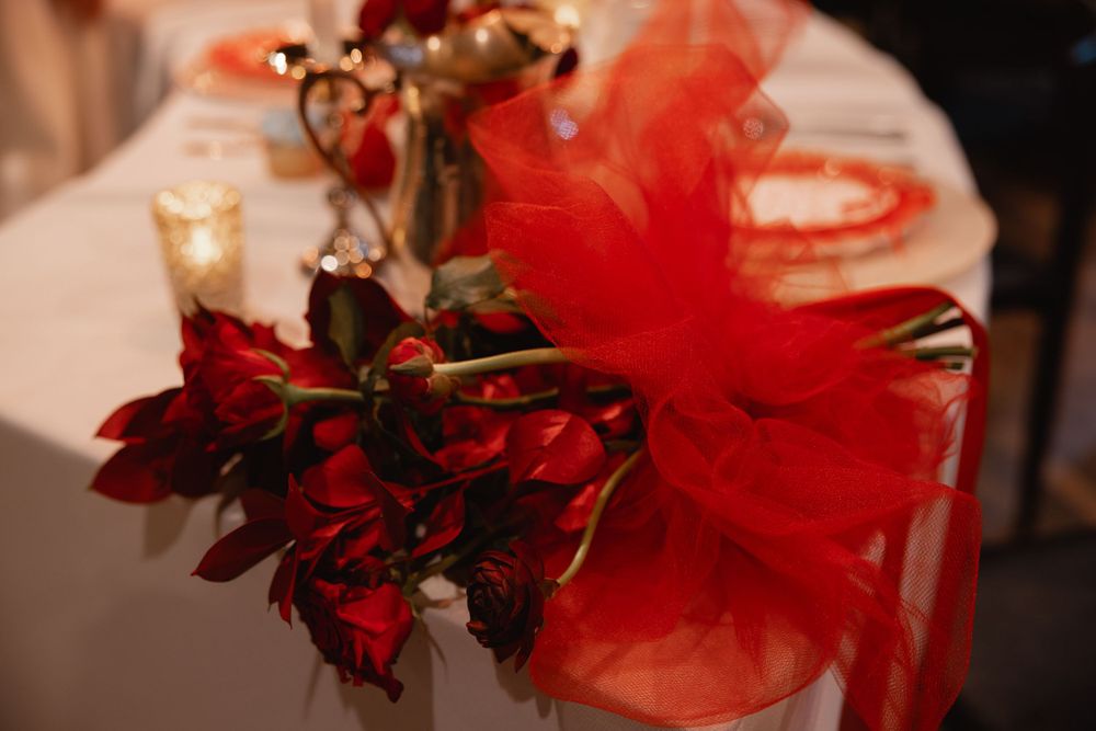 Red roses and tulle bow table decoration with candles for an elegant wedding reception centerpiece.