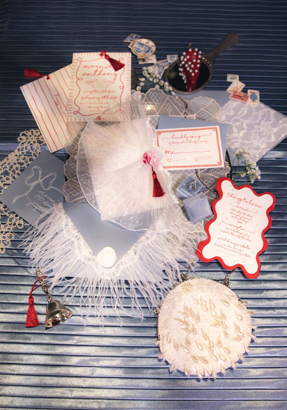 Elegant wedding stationery flat lay with invitations, feathers, lace, and red accents.
