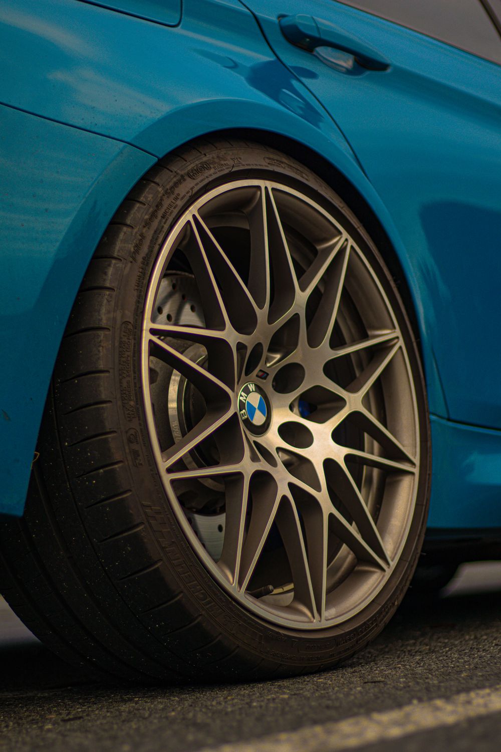 Custom multi-spoke alloy wheels on a blue BMW M4 showing intricate design details.