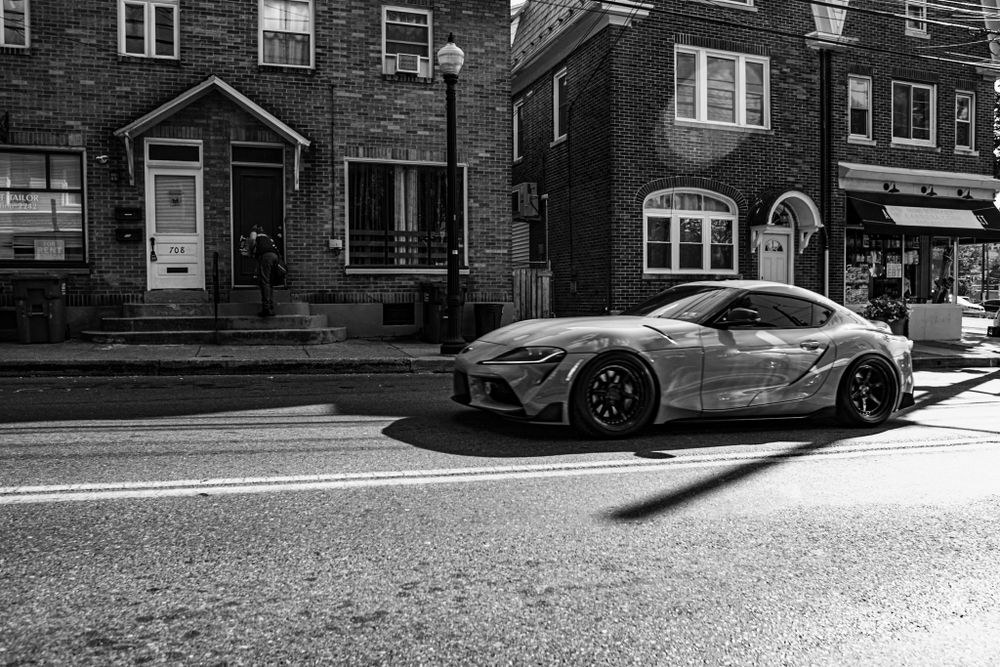 Black and white urban street scene showing parked cars and residential buildings in a city neighborhood.