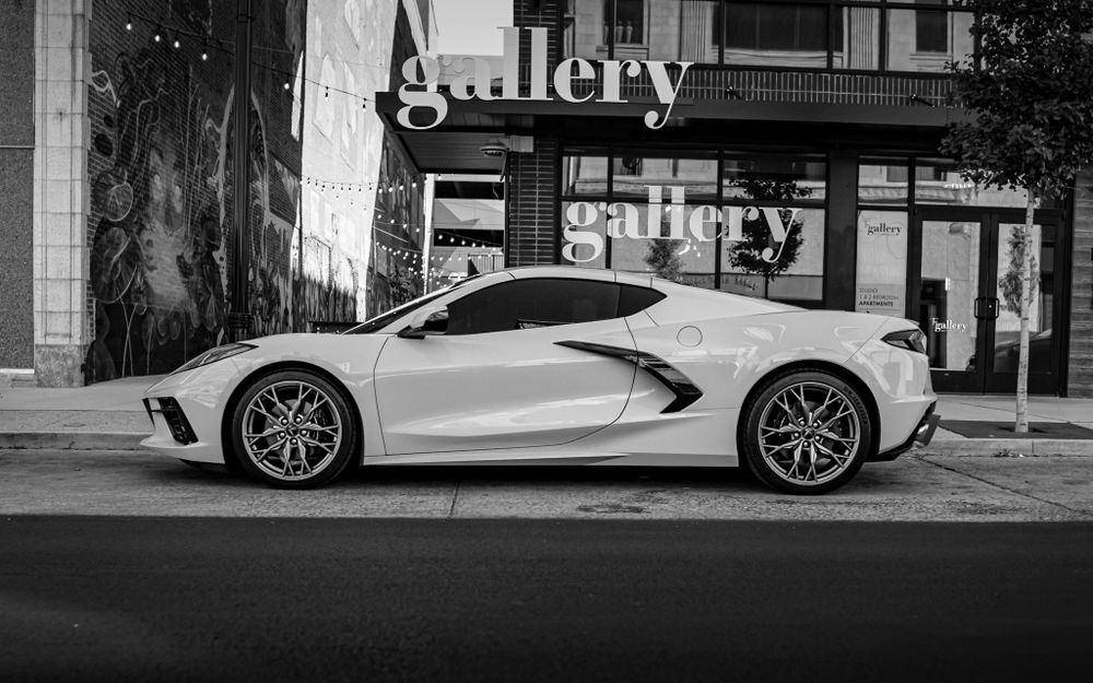 Black and white architectural shots featuring luxury vehicles parked near a gallery entrance.