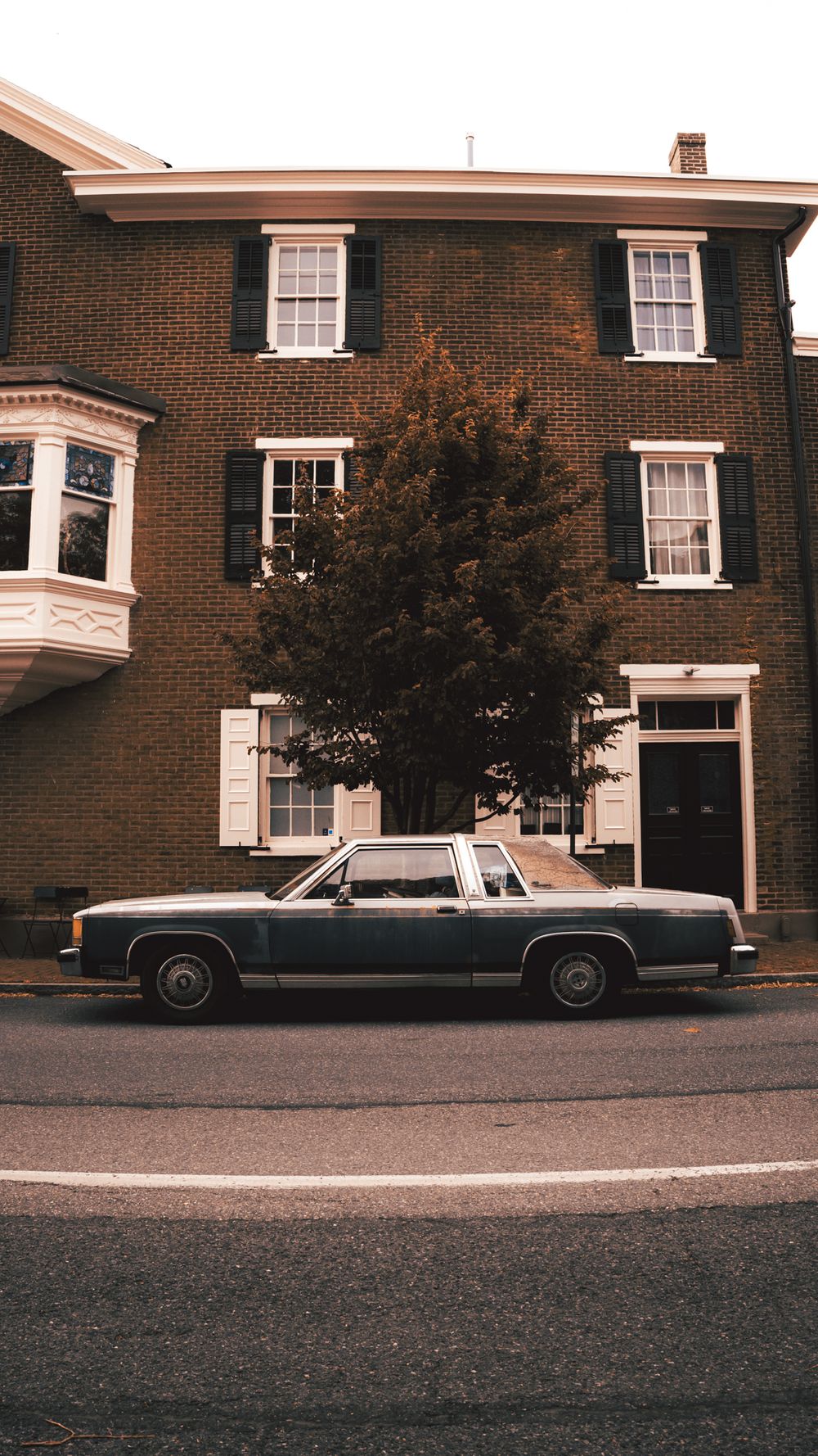 Row of vintage cars parked outside traditional brick townhouses.