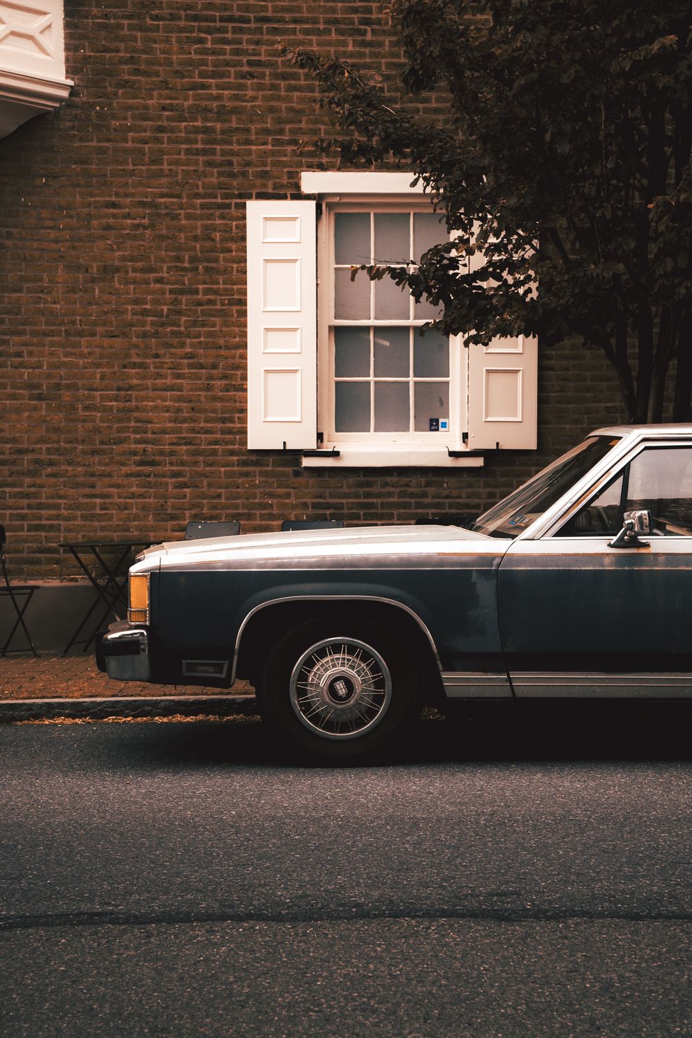 Classic vintage car parked along a brick building with white trim windows.