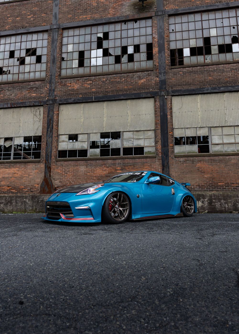 A bright blue sports car parked against an industrial brick building with broken windows.