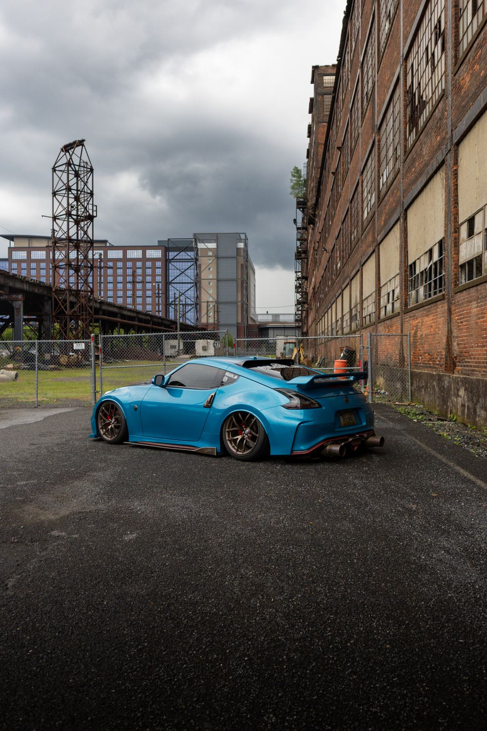 Bright blue sports car parked in front of industrial brick buildings under cloudy skies.