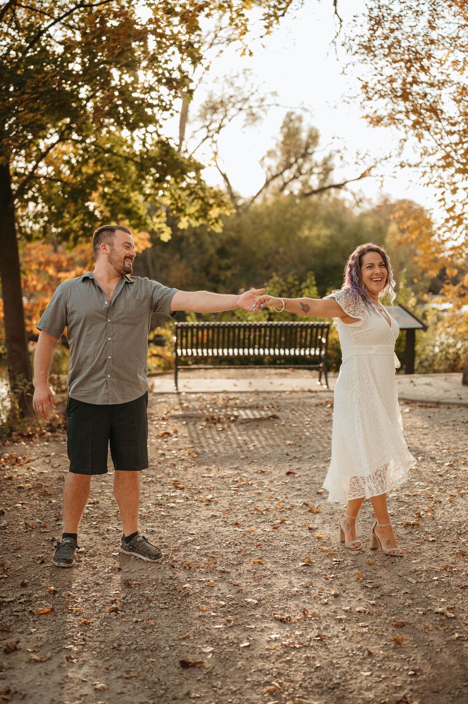 Couple dances playfully in a park during golden hour surrounded by autumn trees.