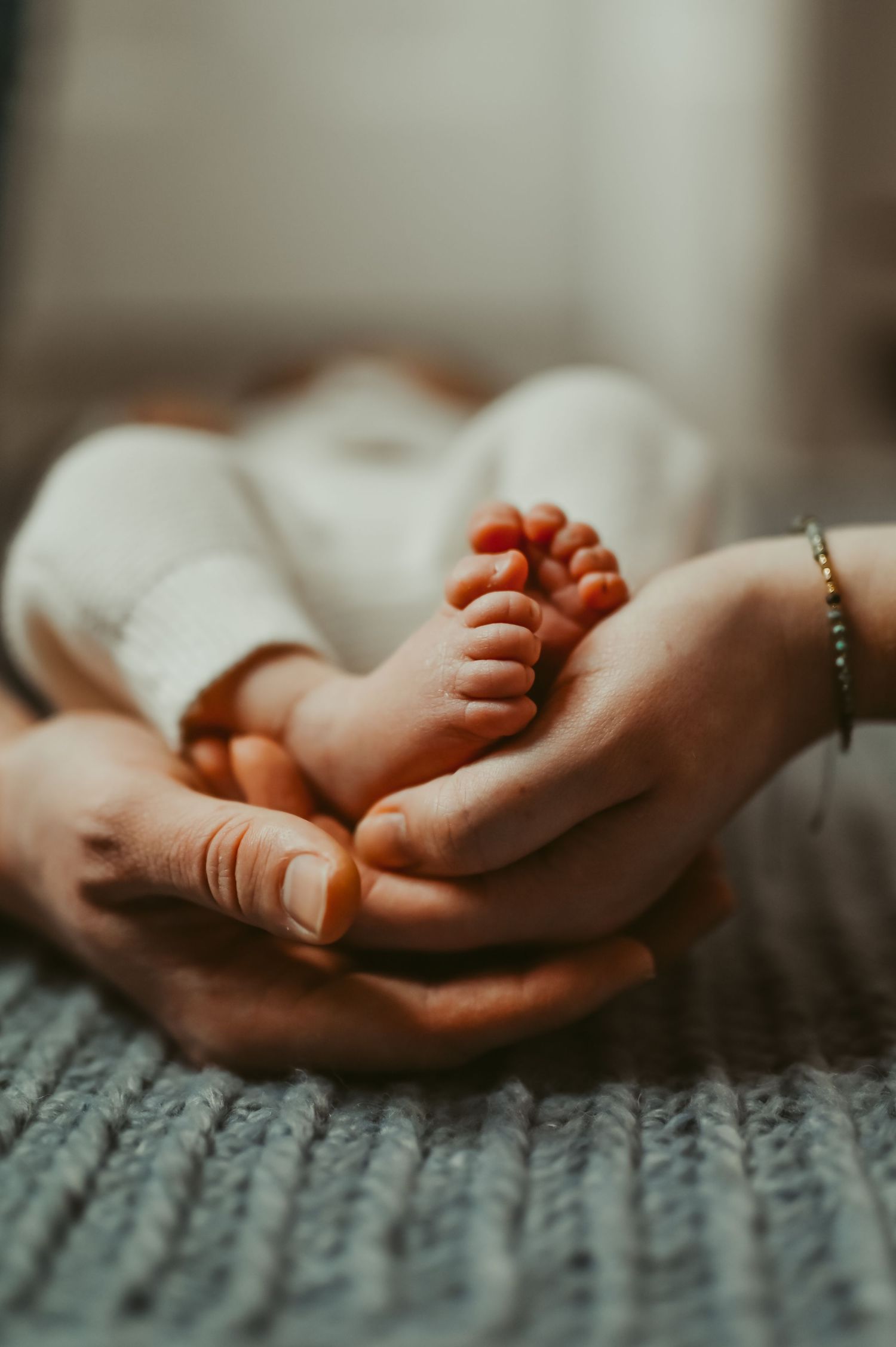 Adult hands gently cradling tiny newborn baby feet, symbolizing parental love and new life. Image taken during an in-home newborn session.
